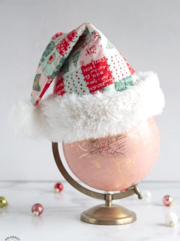 Red, pink and green patchwork santa hat on pink globe